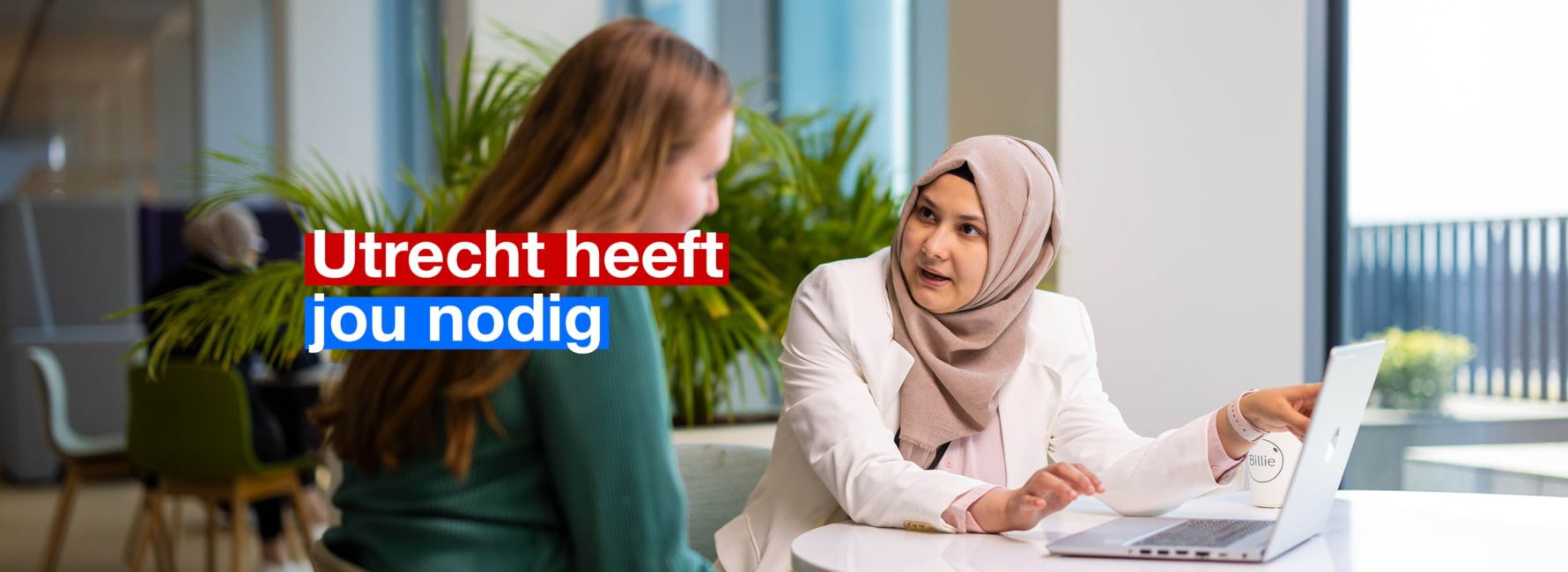 Twee mensen aan een tafel met een laptop. Er wordt uitleg gegeven. In beeld staat de tekst: Utrecht heeft jou nodig.